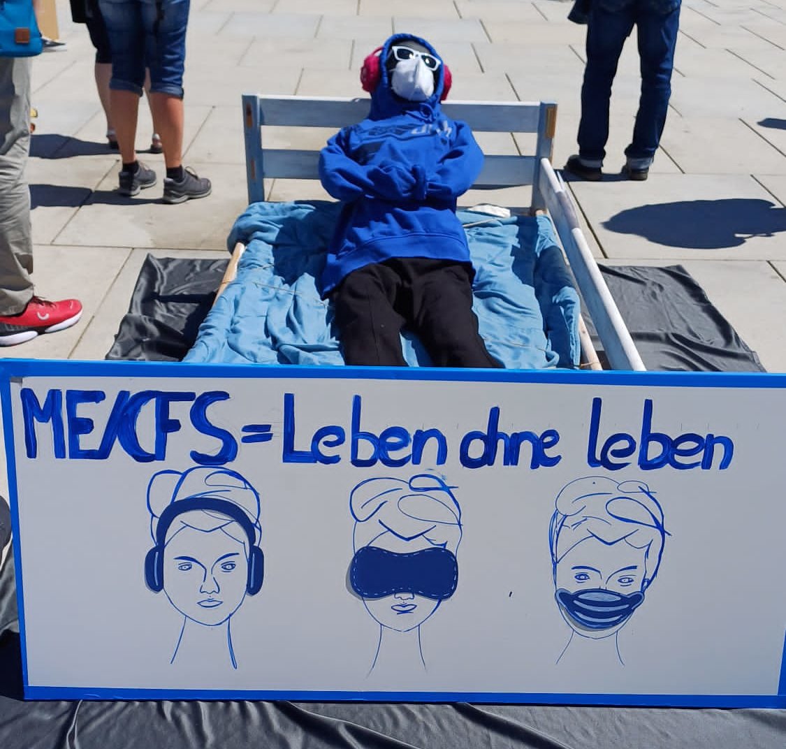 Darstellung einer erkrankten Person mit Gehörschutz, Schlafmaske und FFP2-Maske in einem Bett